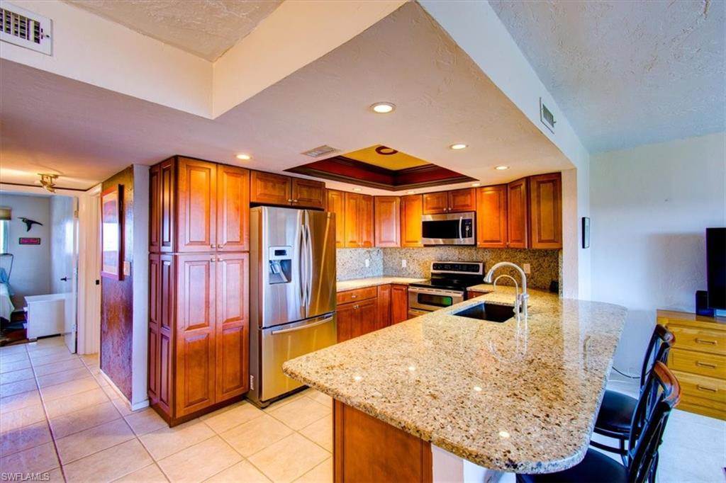 Kitchen with a breakfast bar, sink, kitchen peninsula, stainless steel appliances, and light stone countertops