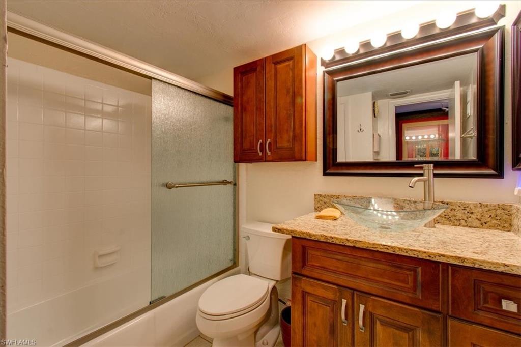 Full bathroom featuring shower / bath combination with glass door, a textured ceiling, vanity, and toilet