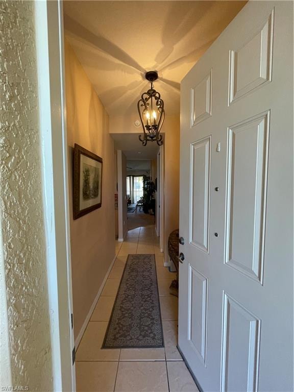 Corridor featuring light tile patterned floors and an inviting chandelier