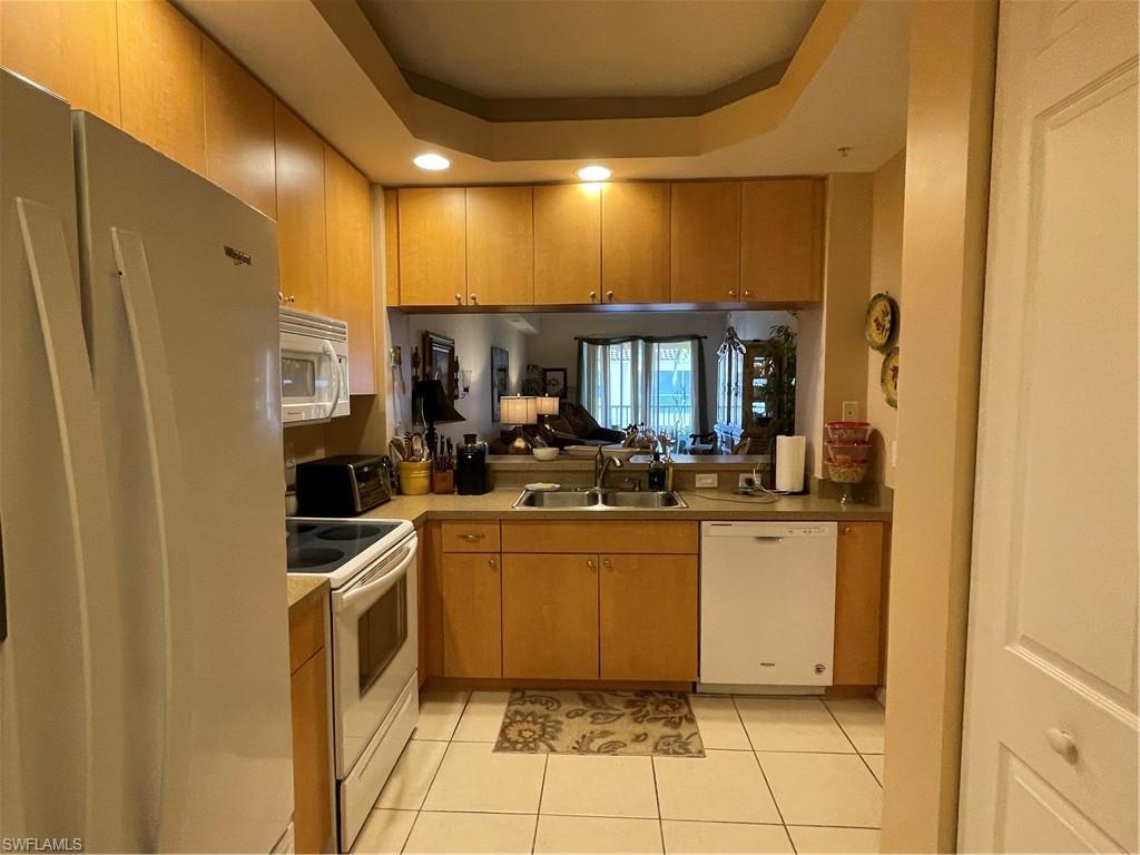 Kitchen featuring a raised ceiling, dishwashing machine, fridge, range, and sink