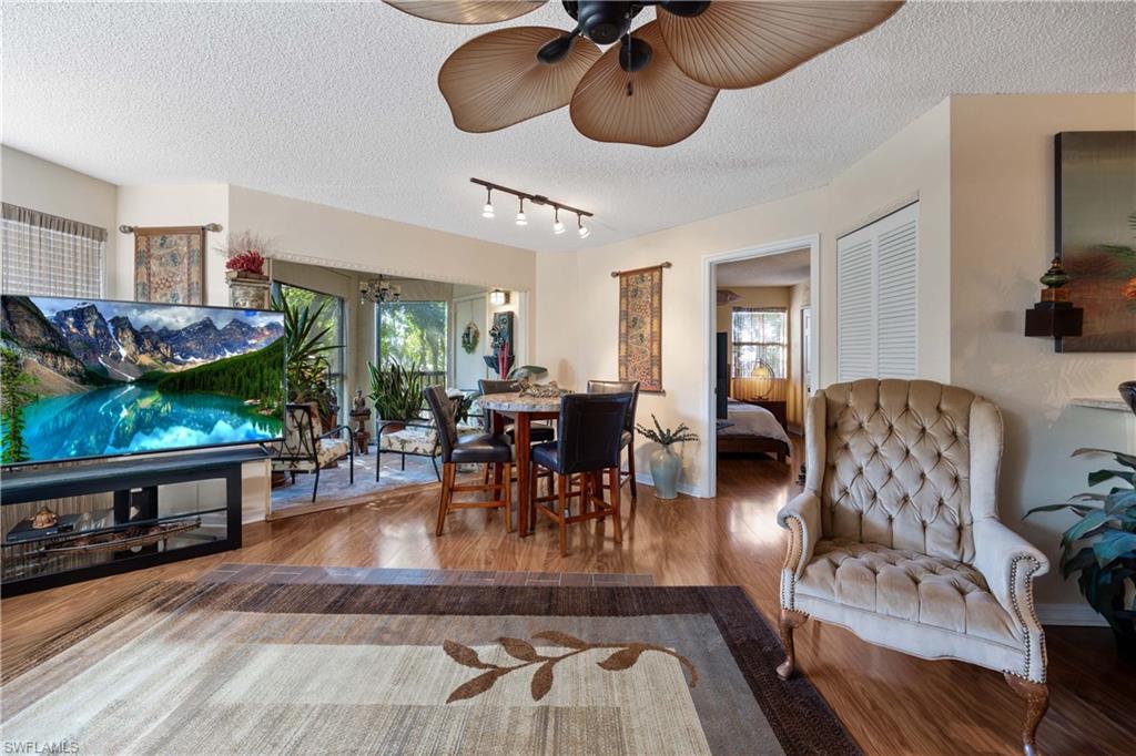 Living room featuring rail lighting, ceiling fan, wood-type flooring, and a textured ceiling
