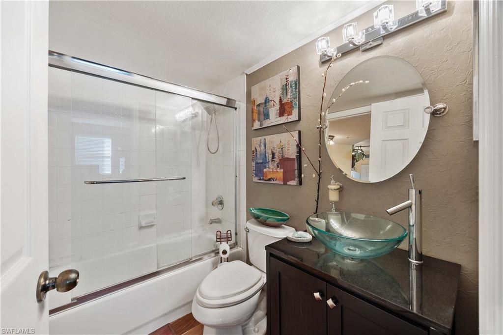 Full bathroom featuring vanity, enclosed tub / shower combo, toilet, and a textured ceiling