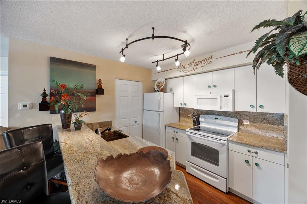 Kitchen with kitchen peninsula, white cabinets, hardwood / wood-style floors, sink, and white appliances