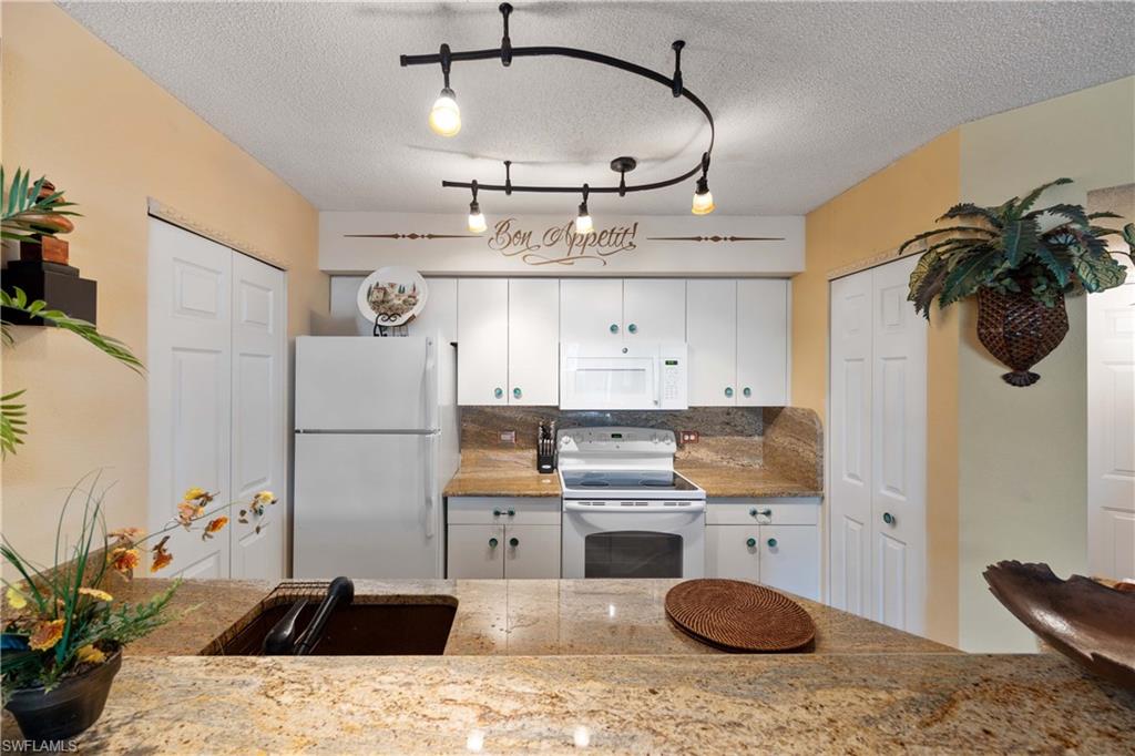 Kitchen featuring white cabinetry, a textured ceiling, and white appliances