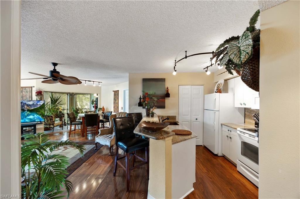 Kitchen with dark hardwood / wood-style floors, a kitchen bar, white cabinets, a textured ceiling, and white appliances