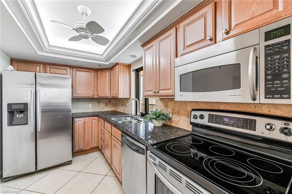 Kitchen with light tile patterned floors, stainless steel appliances, dark stone counters, sink, and a raised ceiling