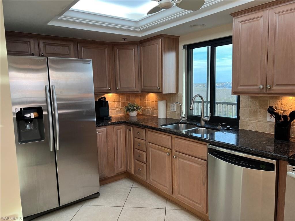 Kitchen featuring sink, a tray ceiling, stainless steel appliances, and dark stone counters