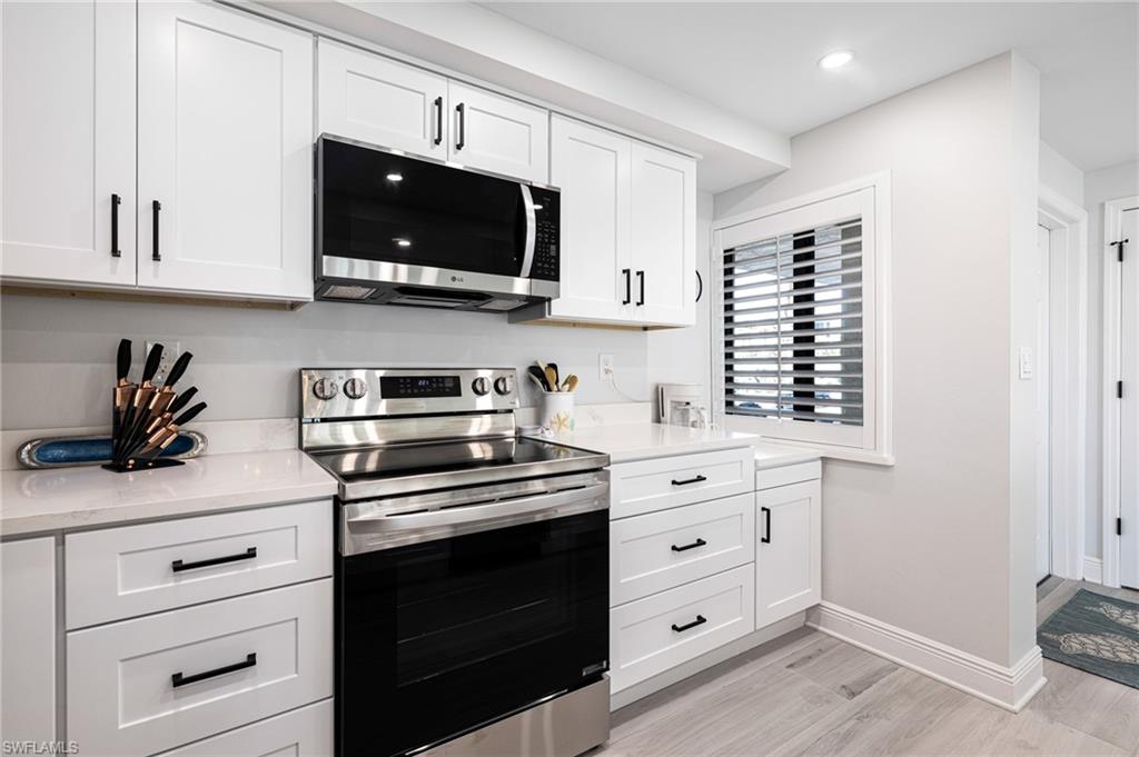 Kitchen featuring light stone countertops, white cabinets, stainless steel appliances, and light wood-type flooring