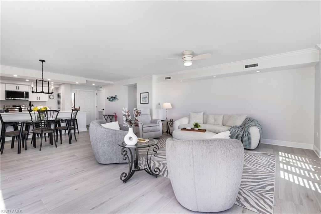 Living room with light hardwood / wood-style floors, crown molding, and ceiling fan with notable chandelier