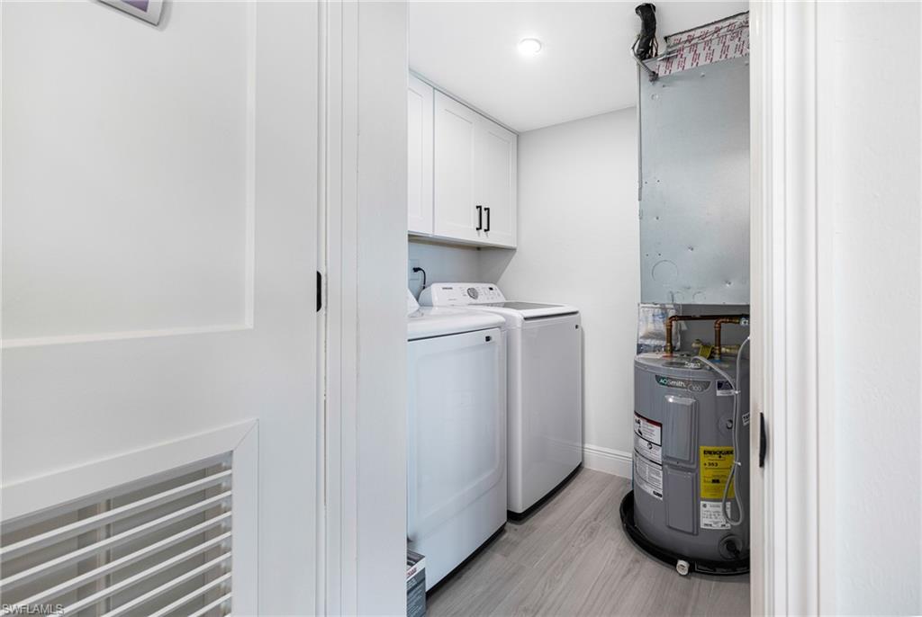 Laundry room with cabinets, washer and dryer, electric water heater, and light hardwood / wood-style floors