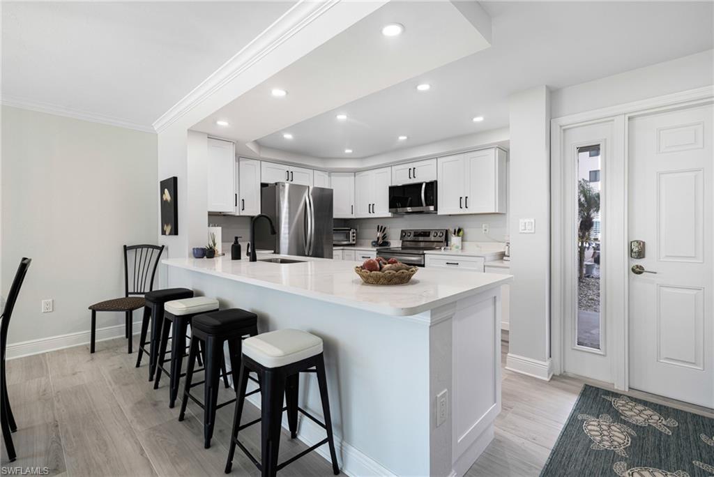 Kitchen featuring a kitchen bar, kitchen peninsula, stainless steel appliances, white cabinets, and light hardwood / wood-style flooring