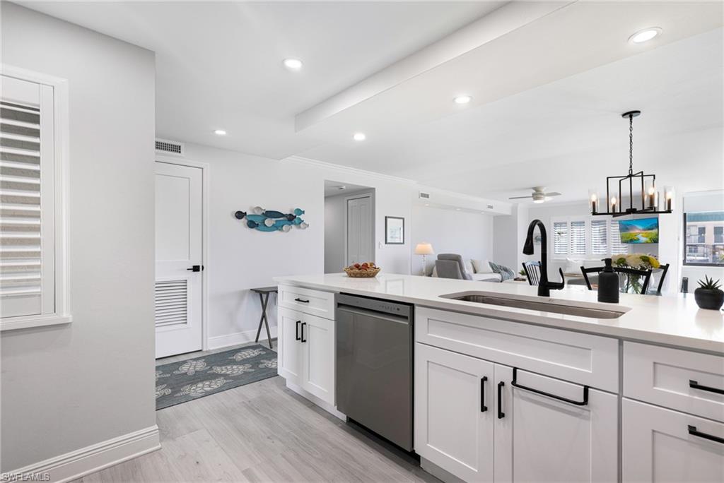 Kitchen featuring sink, light hardwood / wood-style floors, decorative light fixtures, stainless steel dishwasher, and white cabinets
