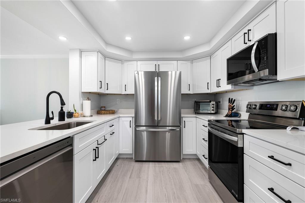 Kitchen with appliances with stainless steel finishes, sink, white cabinetry, ornamental molding, and light hardwood / wood-style flooring