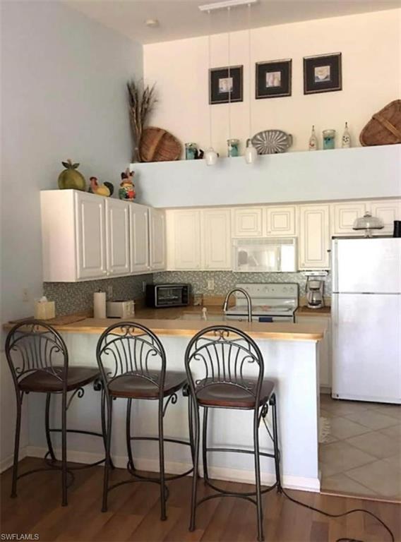 Kitchen with a breakfast bar area, kitchen peninsula, backsplash, and white appliances