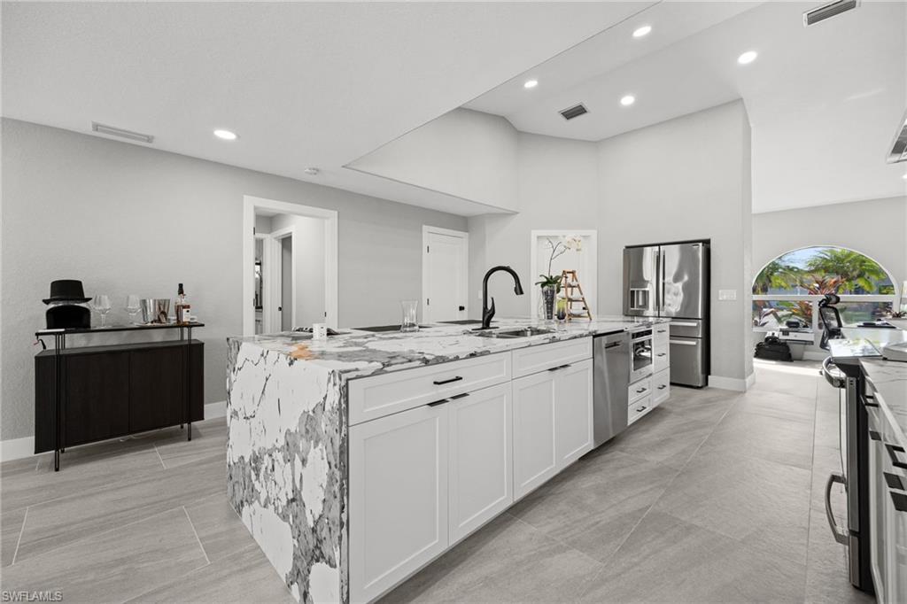 Kitchen featuring an expansive island with waterfall-edge countertop, stainless steel appliances, recessed lighting, and tile flooring