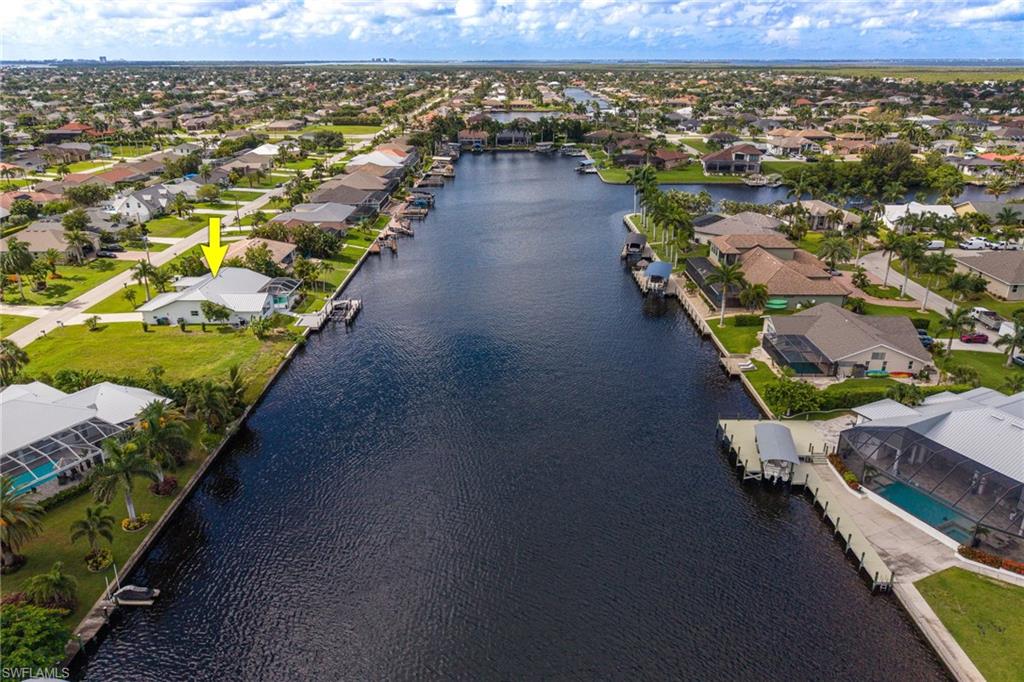 Waterfront property with direct canal access, an attached private dock, a screened-in pool enclosure, and an expansive manicured lawn