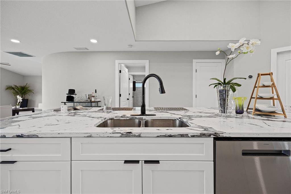 Spacious kitchen island featuring a dual basin sink with a matte black faucet, white shaker-style cabinetry, and a built-in stainless steel dishwasher