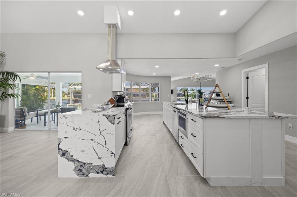 Bright kitchen featuring a waterfall island, recessed lighting, double ovens, and a stainless steel range hood
