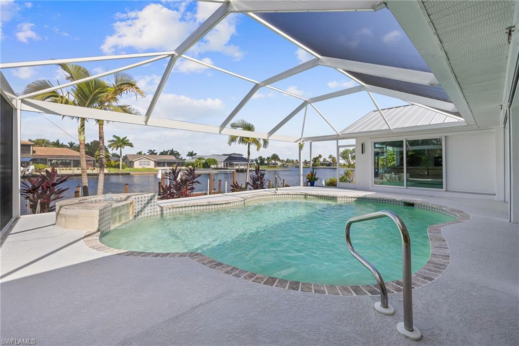Screened-in outdoor living space featuring a freeform swimming pool with integrated spa and canal frontage