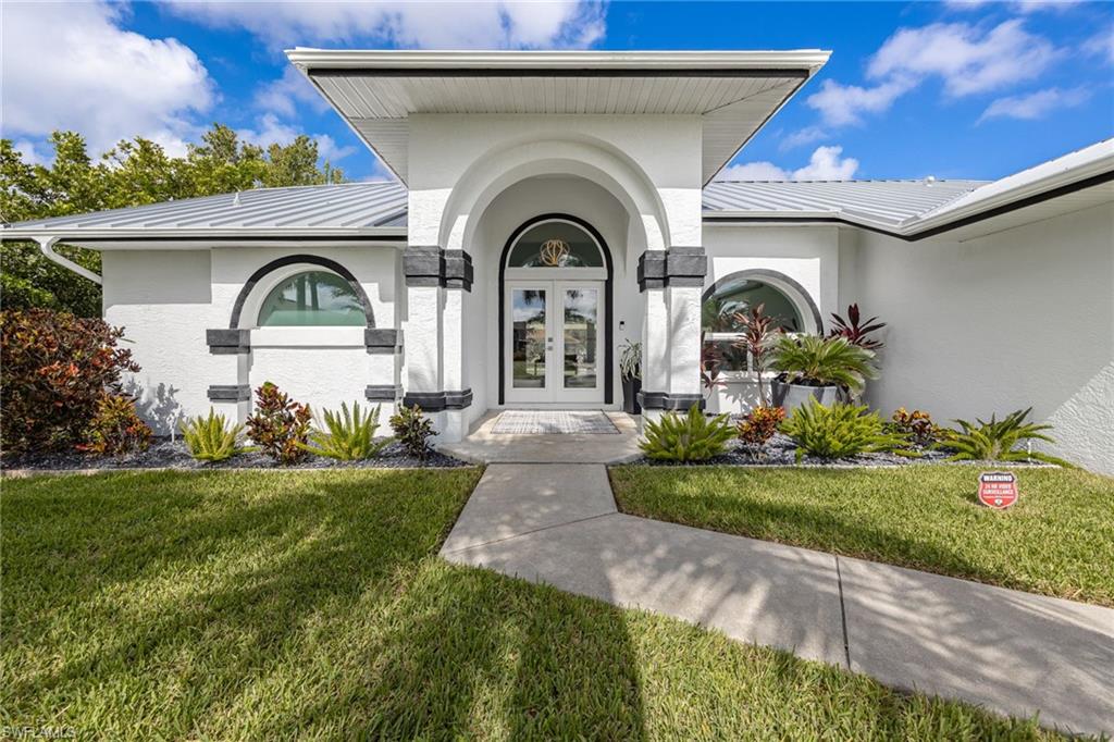 Stucco exterior with metal roof, arched entry, double front doors, and semicircular windows