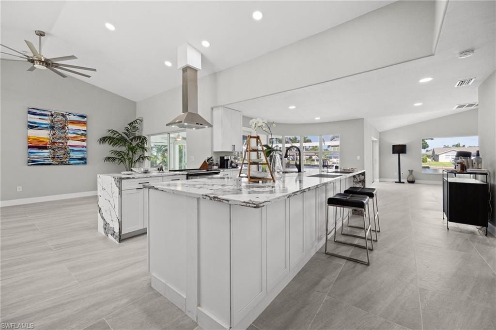 Spacious kitchen with a central island featuring a waterfall edge, stainless steel range hood, paneled cabinetry, and recessed lighting