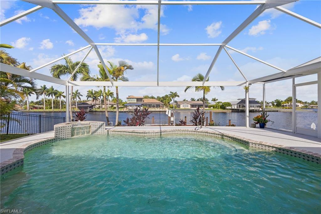 Screened outdoor pool with a waterfall feature, surrounding paver patio, and canal access