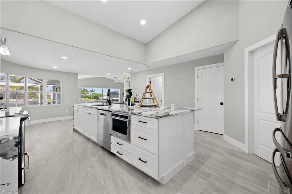 Expansive kitchen with a large center island, integrated stainless steel appliances, modern recessed lighting, and tile flooring