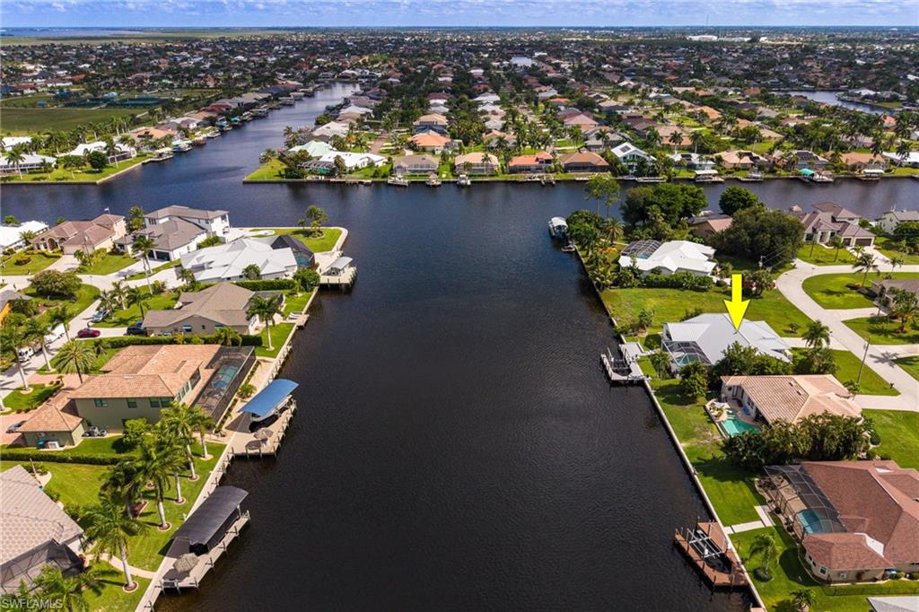 Waterfront property featuring a private boat dock, lush green lawn, and mature palm trees