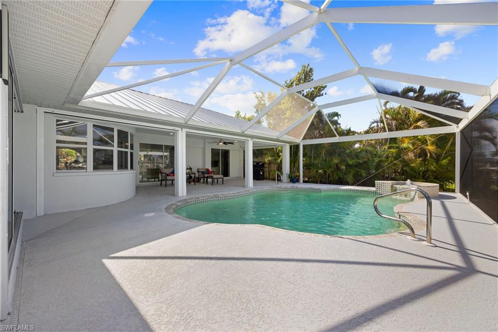 Screened-in outdoor living space with a curved swimming pool, extensive concrete decking, and a covered patio area