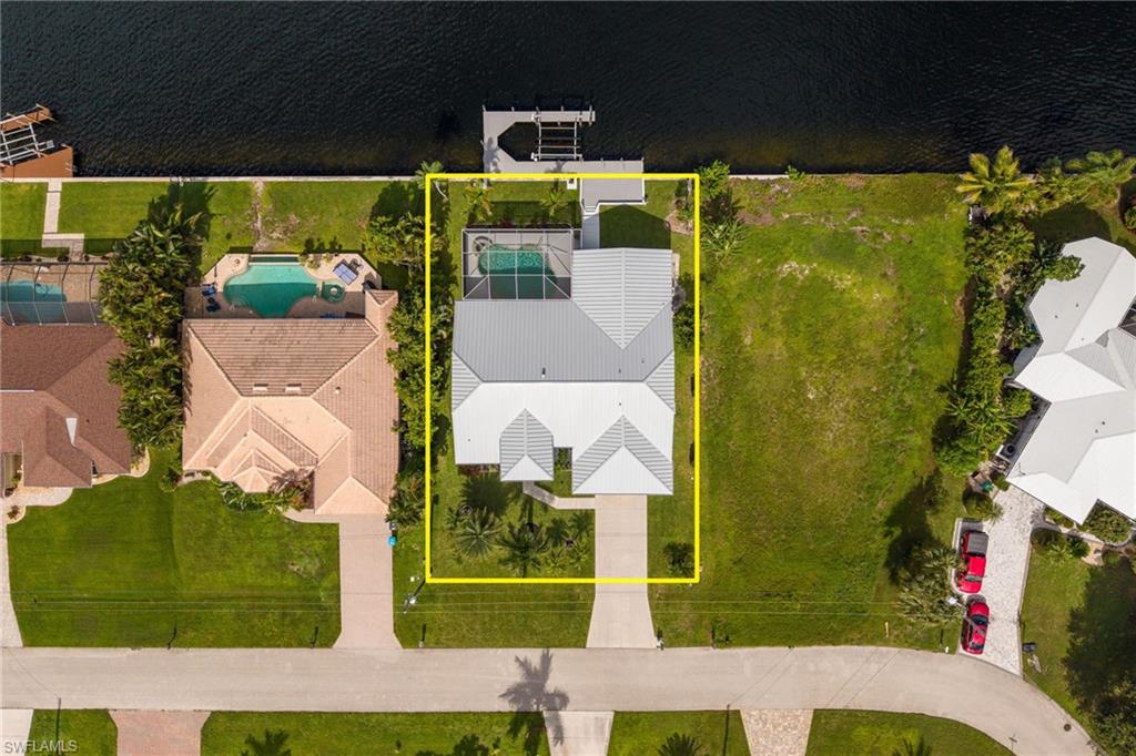 Waterfront property featuring a private boat dock, a screened-in swimming pool, a concrete driveway, and a well-maintained lawn