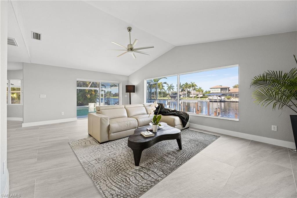 Vaulted ceiling with a ceiling fan, light gray wall paint, large format tile flooring, expansive windows, and a sliding glass door