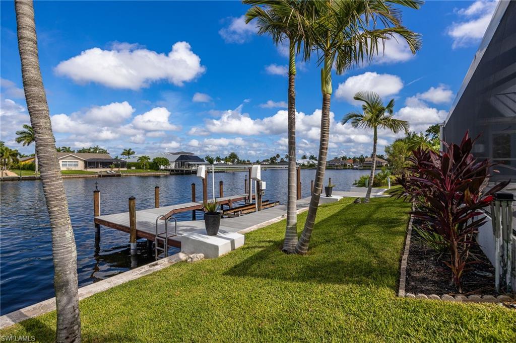 Waterfront property featuring a private boat dock, lush green lawn, mature palm trees, and established landscaping