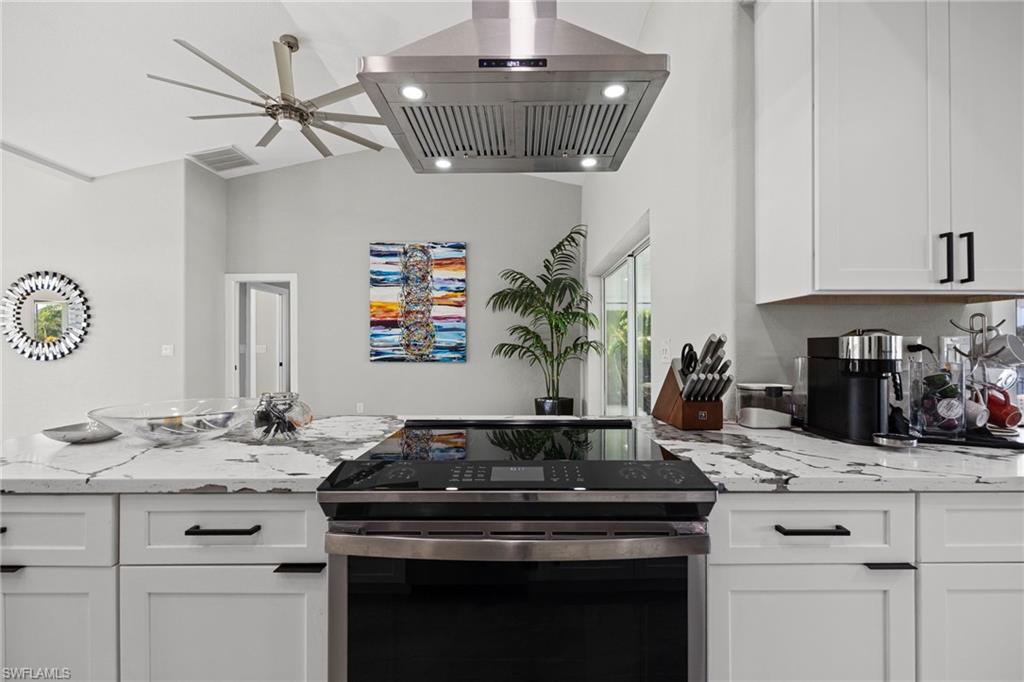 White cabinetry with black hardware, stainless steel range hood, built-in electric range, and light-toned countertops