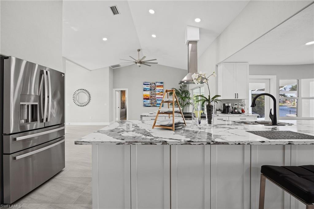 Spacious kitchen featuring an island with a white and gray countertop, white cabinetry, a stainless steel refrigerator, and a stainless steel range hood