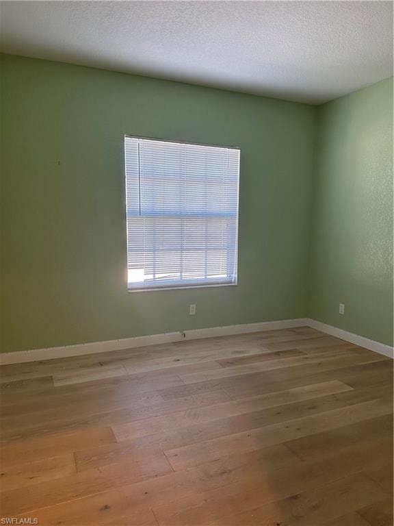 Empty room with light hardwood / wood-style floors and a textured ceiling