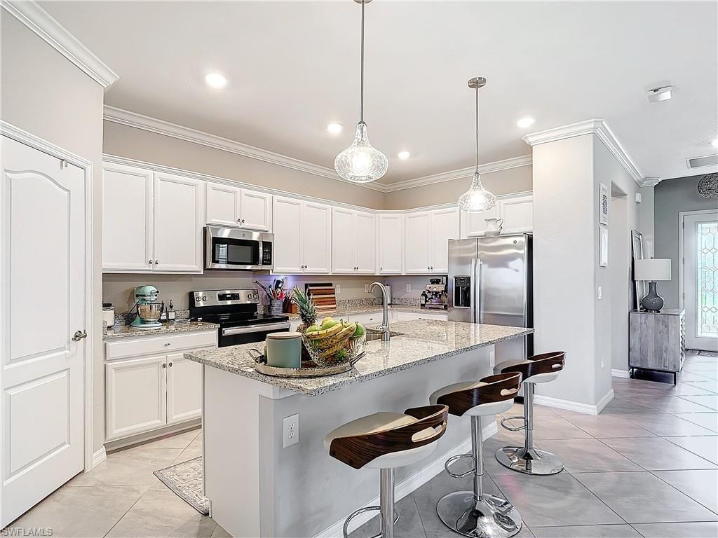Kitchen featuring white cabinetry, appliances with stainless steel finishes, light stone countertops, a kitchen island with sink, and crown molding