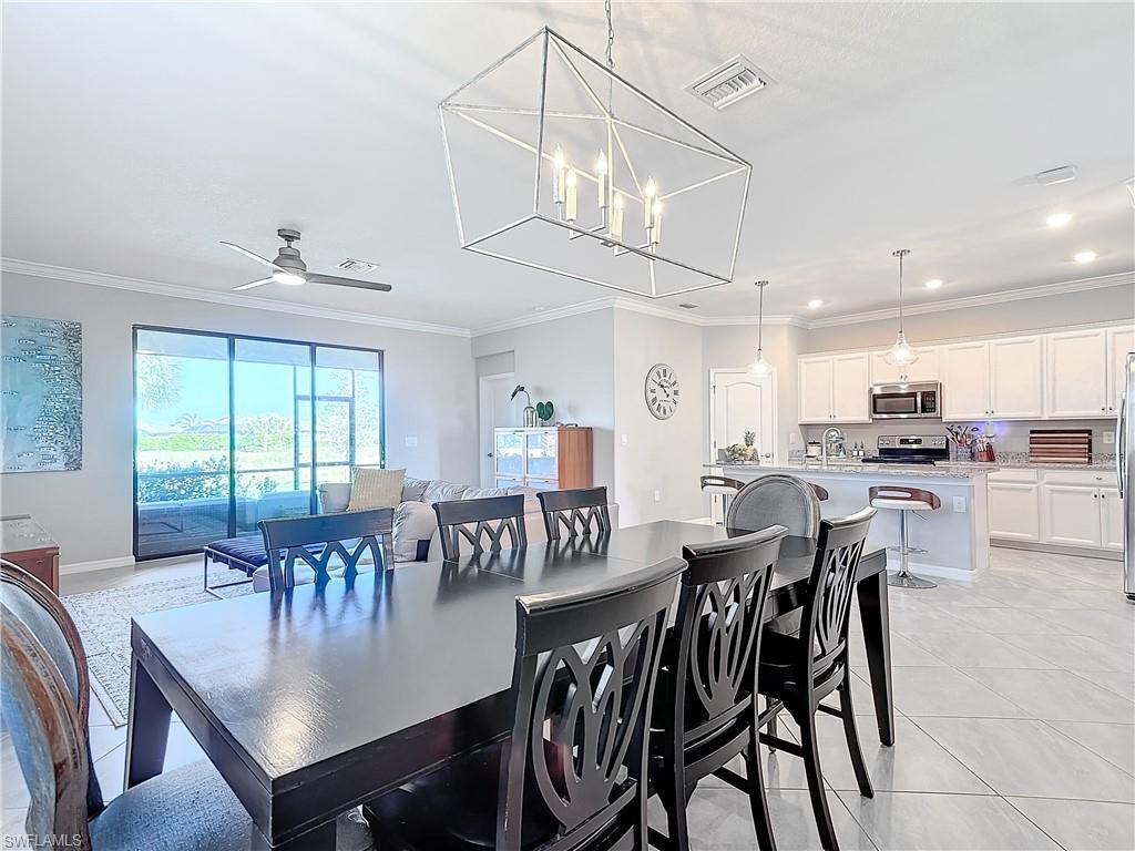 Dining space with light tile patterned floors, crown molding, and ceiling fan with notable chandelier