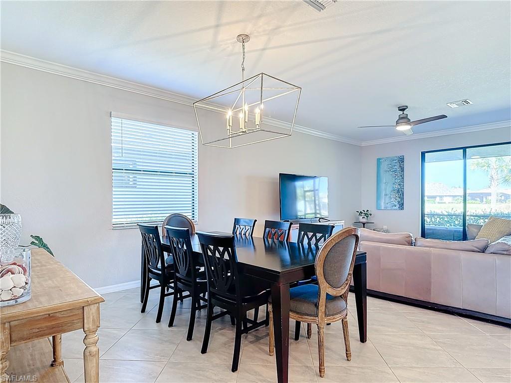 Dining area with ceiling fan with notable chandelier, light tile patterned flooring, and crown molding