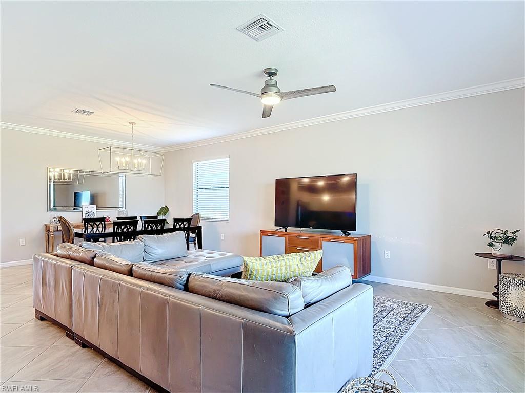 Tiled living room featuring ceiling fan with notable chandelier and crown molding