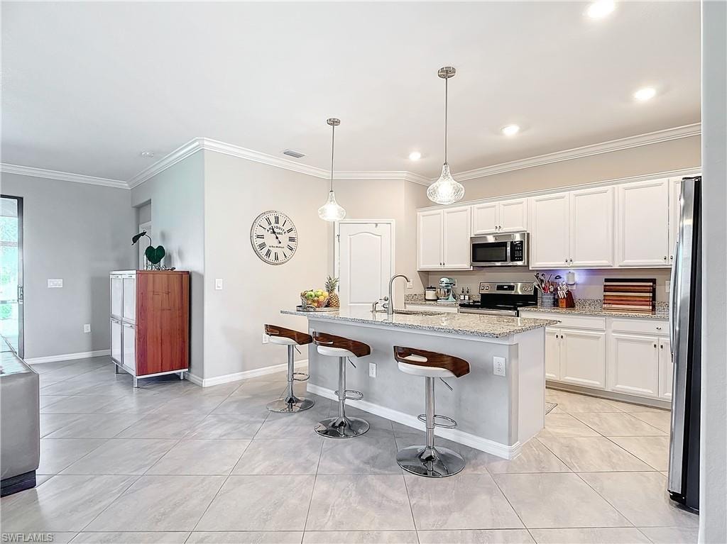 Kitchen featuring white cabinetry, appliances with stainless steel finishes, decorative light fixtures, light stone countertops, and a kitchen island with sink