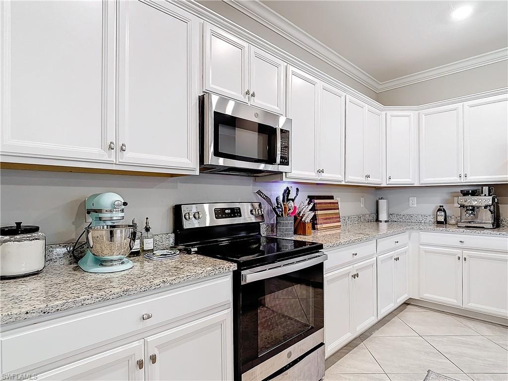 Kitchen with white cabinets, appliances with stainless steel finishes, light stone counters, and crown molding