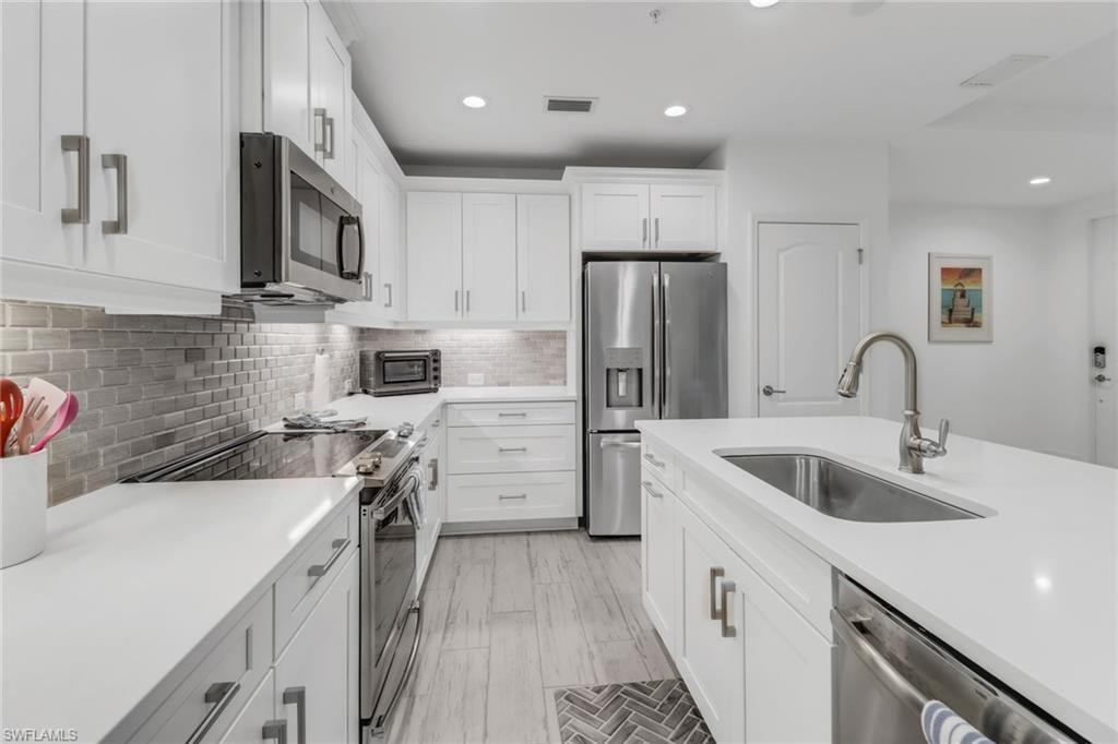 Light, bright kitchen with white cabinetry, stainless steel appliances, decorative backsplash, sink, and under-counter lighting