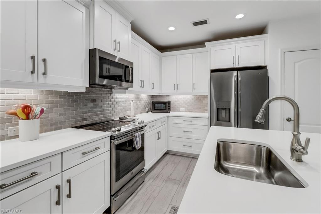 Kitchen with white cabinets, stainless steel appliances, sink, and tile backsplash