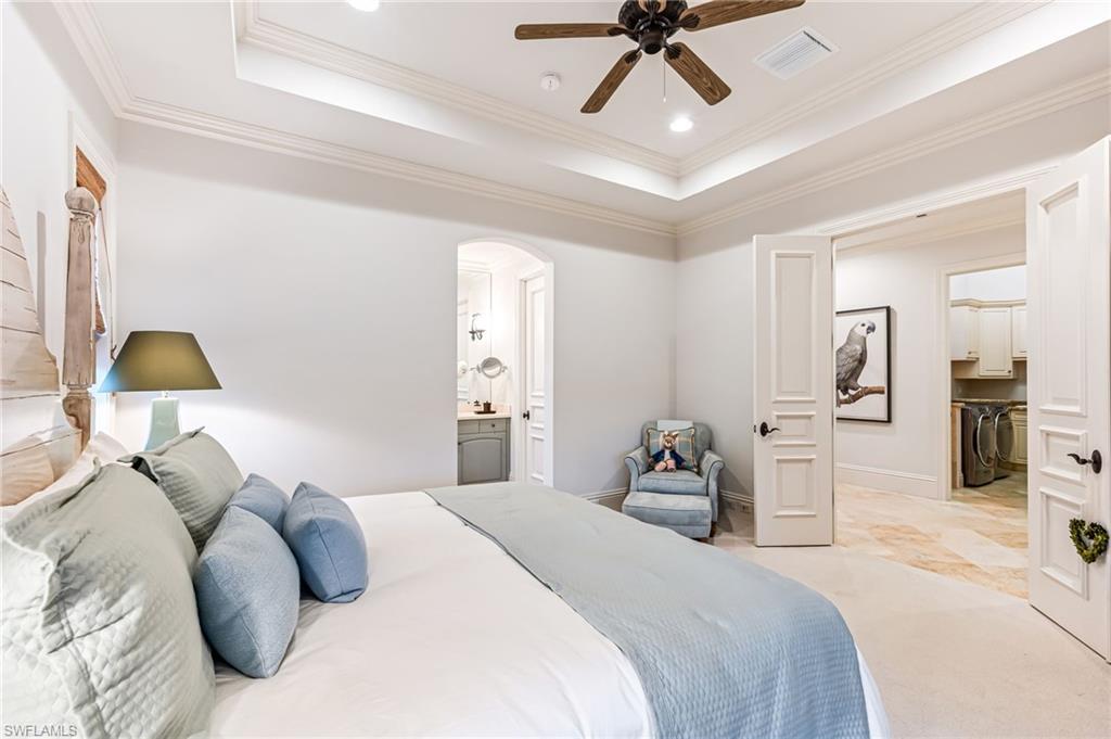 Bedroom featuring ceiling fan, a raised ceiling, ornamental molding, and ensuite bath