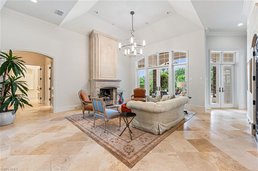 Living room with french doors, a large fireplace, ornamental molding, and a notable chandelier