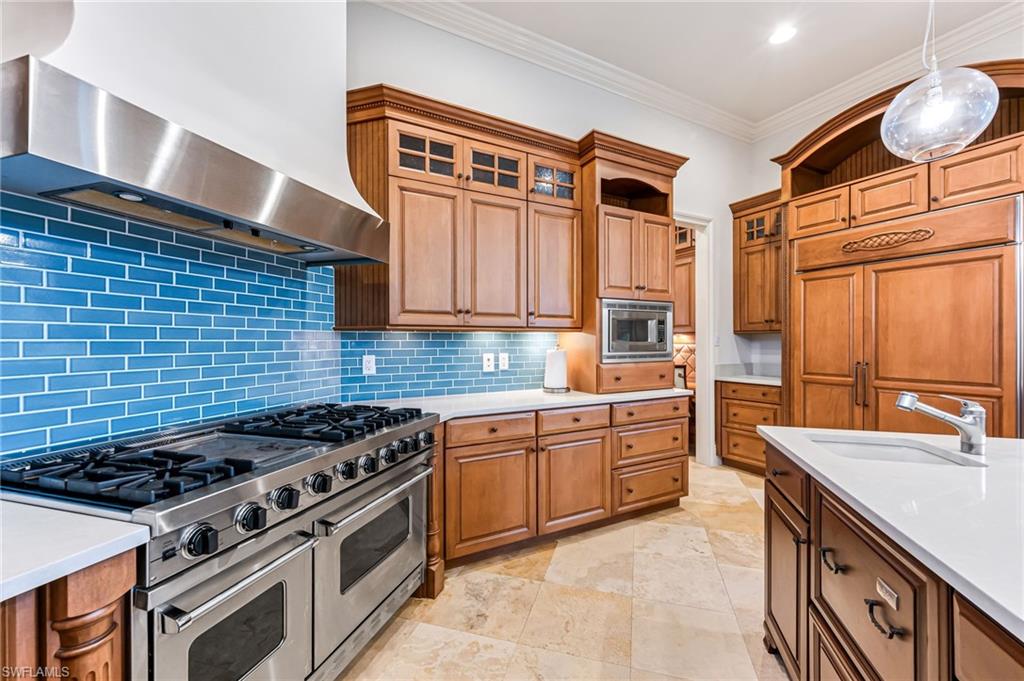Kitchen featuring backsplash, sink, wall chimney range hood, pendant lighting, and built in appliances