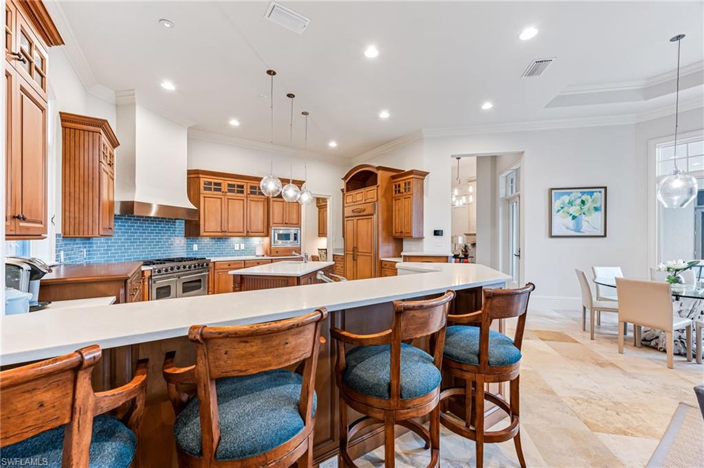 Kitchen with wall chimney exhaust hood, pendant lighting, a spacious island, appliances with stainless steel finishes, and ornamental molding