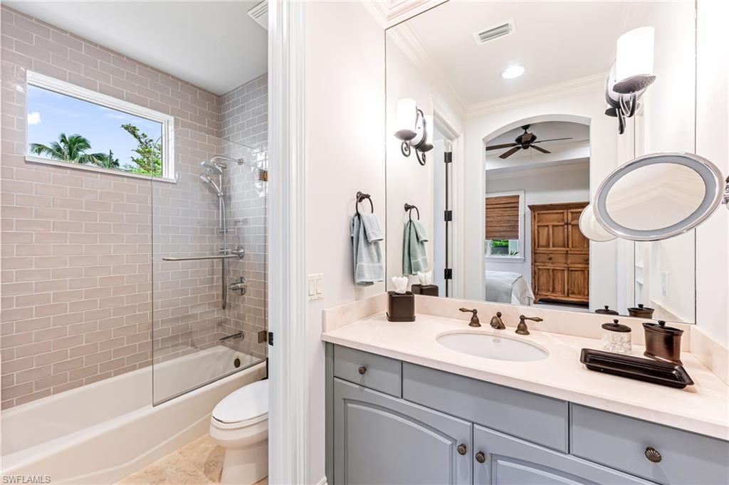Full bathroom with vanity, ceiling fan, tiled shower / bath combo, toilet, and ornamental molding