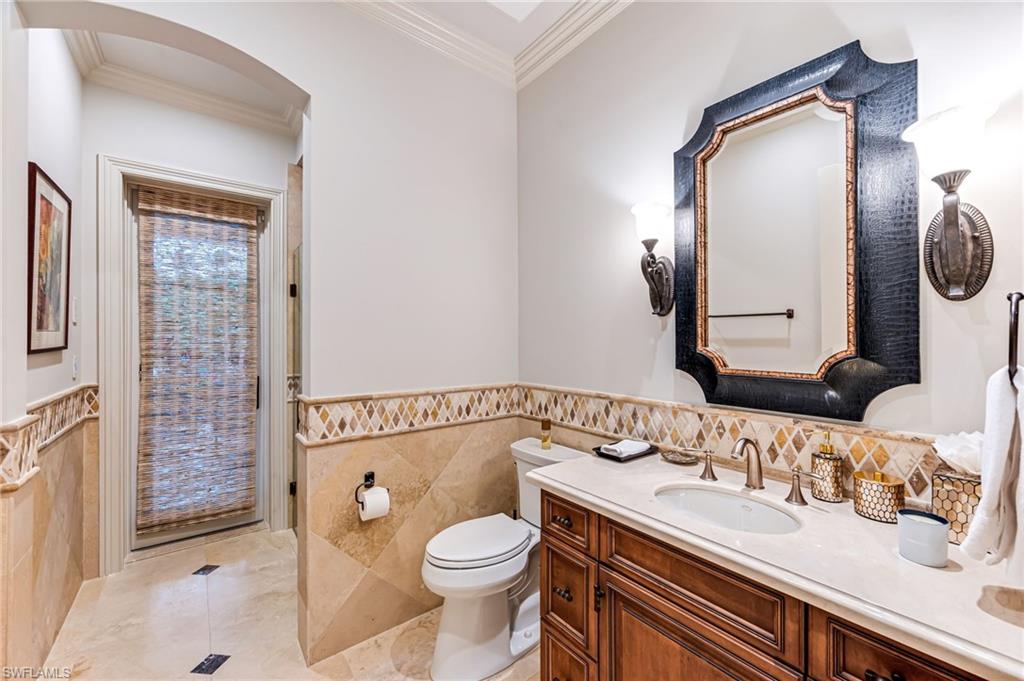 Bathroom with vanity, toilet, ornamental molding, and tile walls