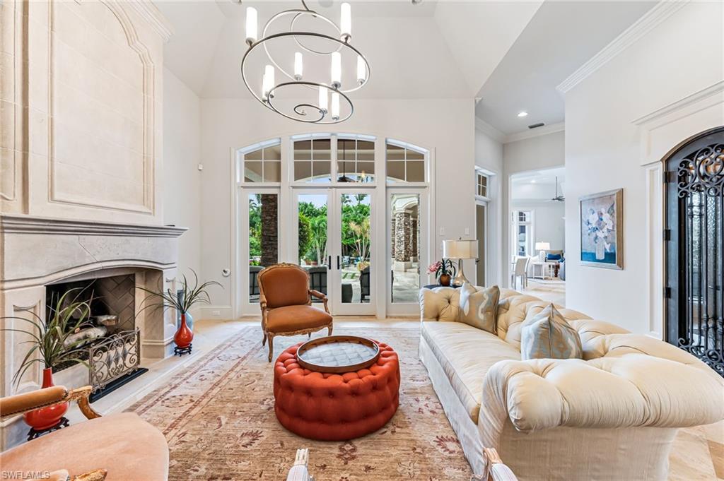 Living room with high vaulted ceiling, french doors, a premium fireplace, ornamental molding, and a chandelier